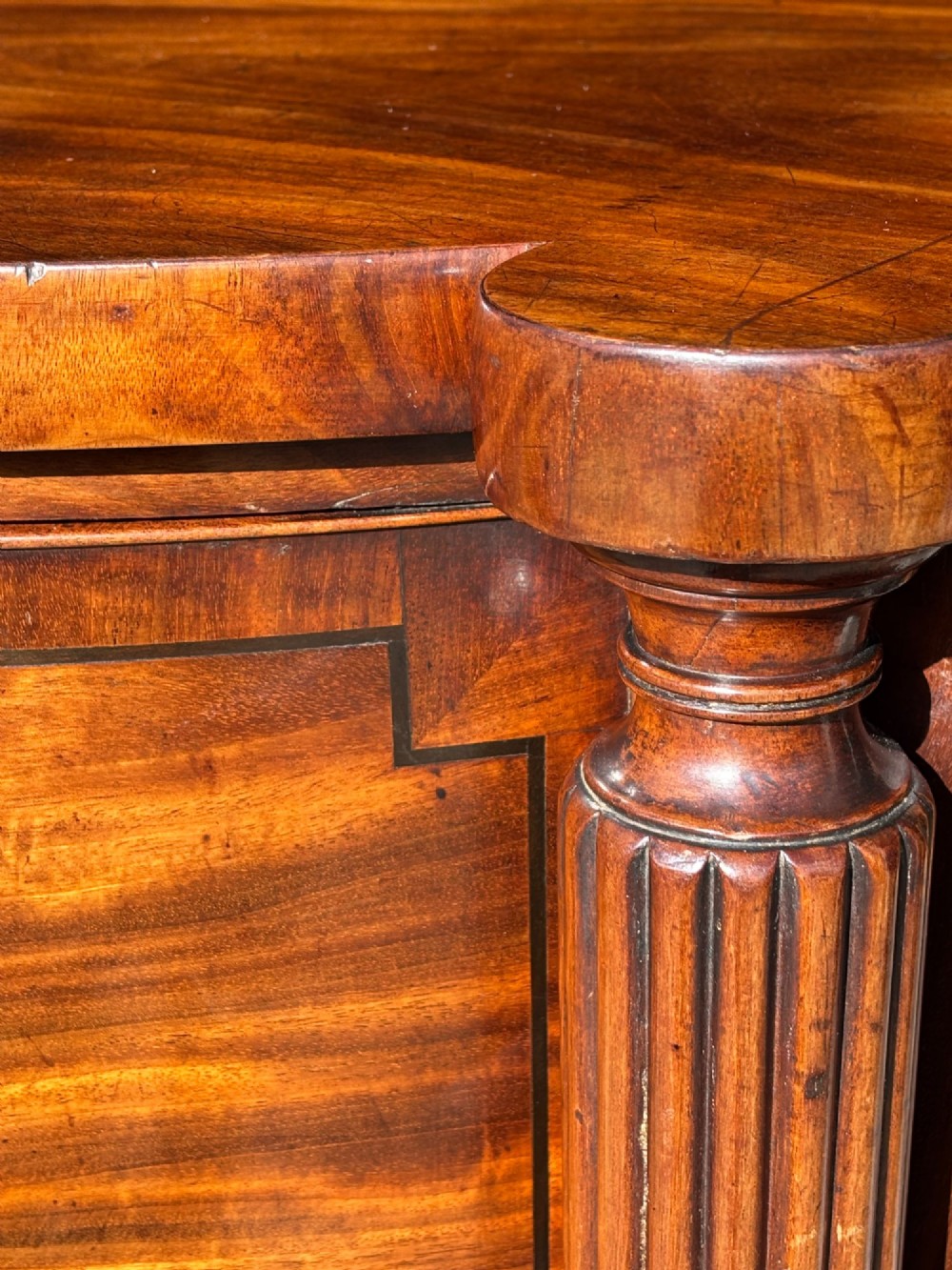 An antique 19th-century William IV mahogany sideboard featuring reeded fluted legs, line inlay, and a central drawer above an arched recess. View X