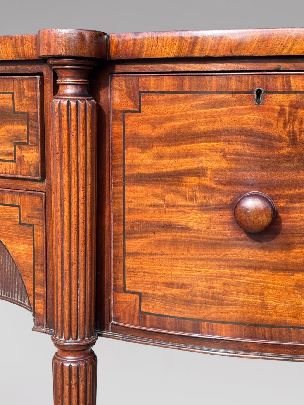 An antique 19th-century William IV mahogany sideboard featuring reeded fluted legs, line inlay, and a central drawer above an arched recess. View XII