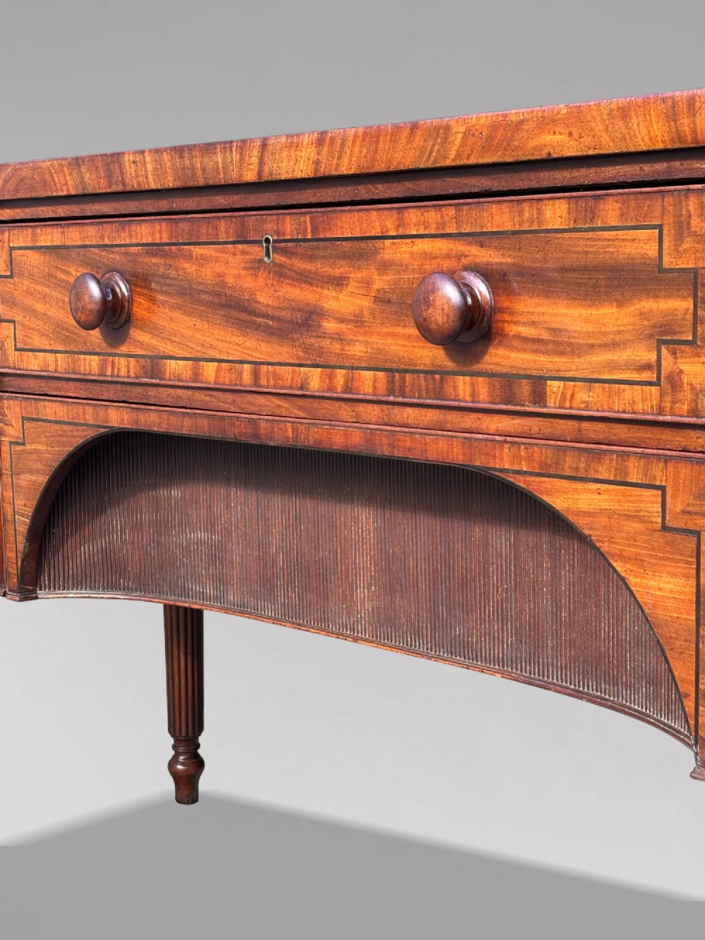 An antique 19th-century William IV mahogany sideboard featuring reeded fluted legs, line inlay, and a central drawer above an arched recess. View XIII