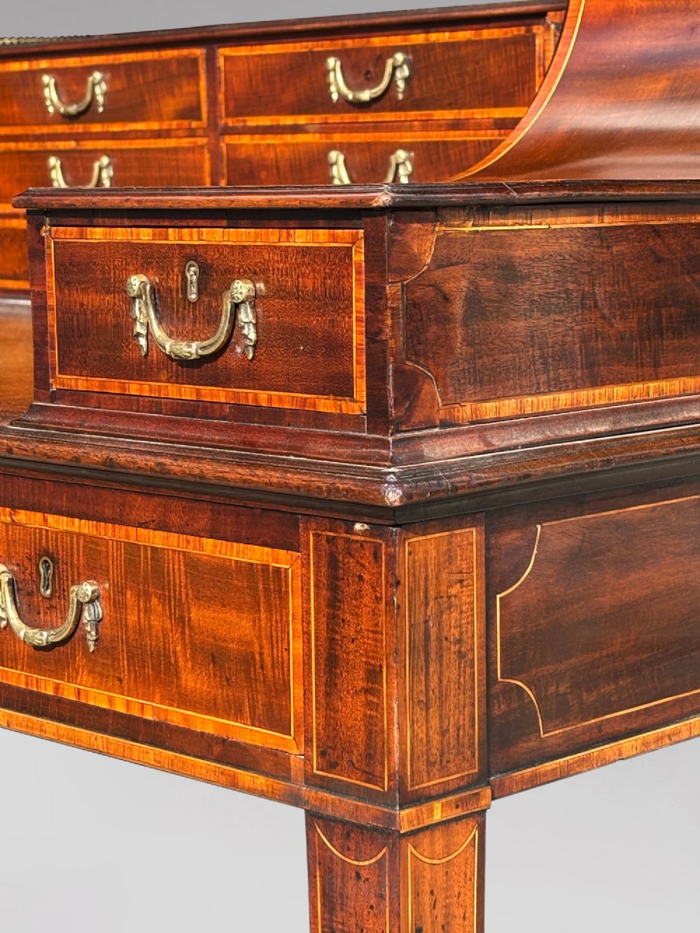 An 18th-century George III mahogany Carlton House desk with inlaid marquetry, a leather writing surface, small upper drawers, and tapered legs on brass castors. View X