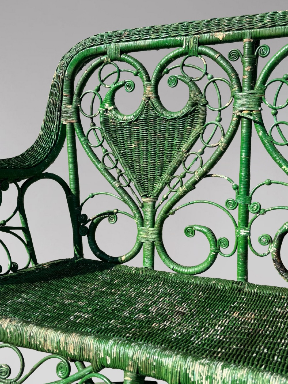 A French green painted wicker bench featuring two heart-shaped openwork back panels and curved armrests. View V