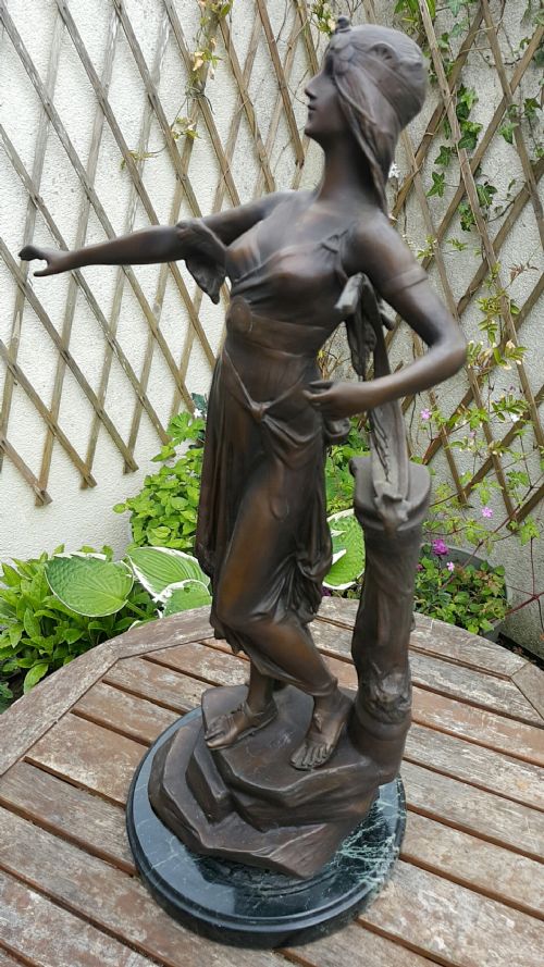 fig 1. A dark patinated bronze sculpture of Salome draped in classical robes holding a lyre, positioned on a rounded dark marble base.