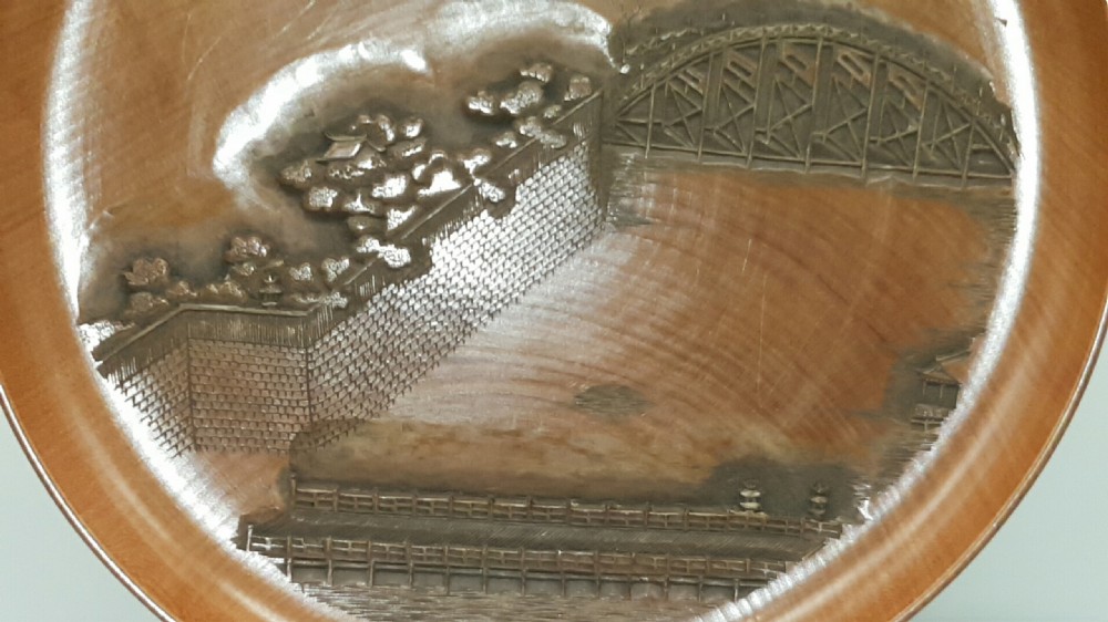 A stacked set of five shallow circular warm brown wood trays featuring low-relief carvings of traditional Japanese landscapes. View III