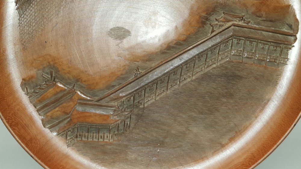 A stacked set of five shallow circular warm brown wood trays featuring low-relief carvings of traditional Japanese landscapes. View VII