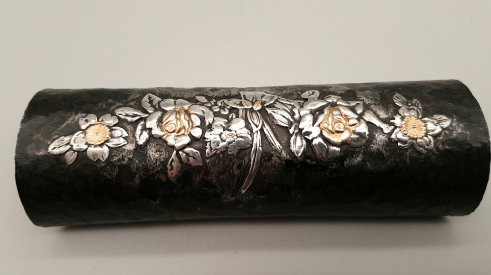 A cylindrical dark iron tea scoop featuring intricate silver and gold floral inlays across the surface. View II