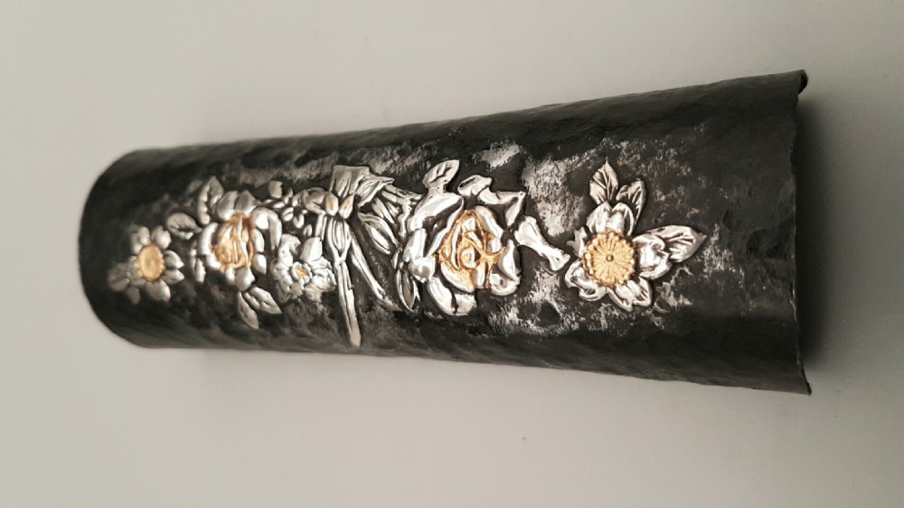 A cylindrical dark iron tea scoop featuring intricate silver and gold floral inlays across the surface. View III