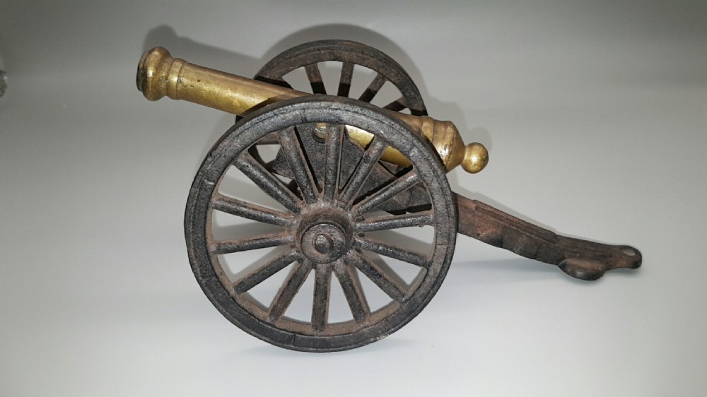 A 19th-century scale model of a Gribeauval field gun featuring a turned bronze barrel mounted on a dark cast iron carriage with spoked wheels.
