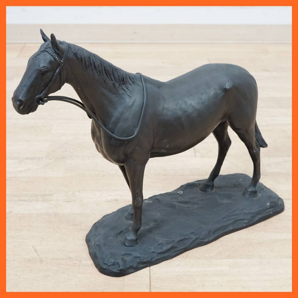 A dark patinated bronze sculpture of a standing horse on an integral rocky base.