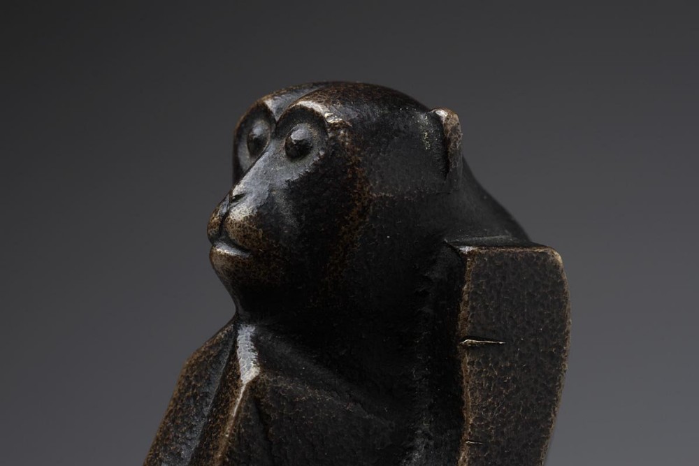 A close-up studio shot of a dark brown bronze monkey paperweight showing detailed facial features and textured fur.