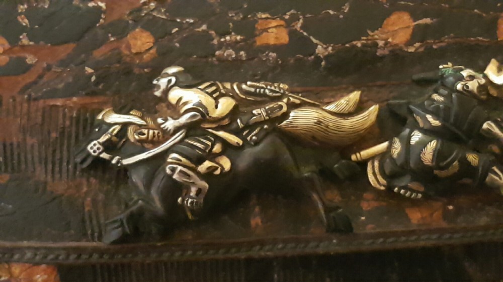 A rectangular dark brown tooled leather pouch featuring a metallic clasp decorated with embossed samurai figures on horseback in gold and silver. View XII