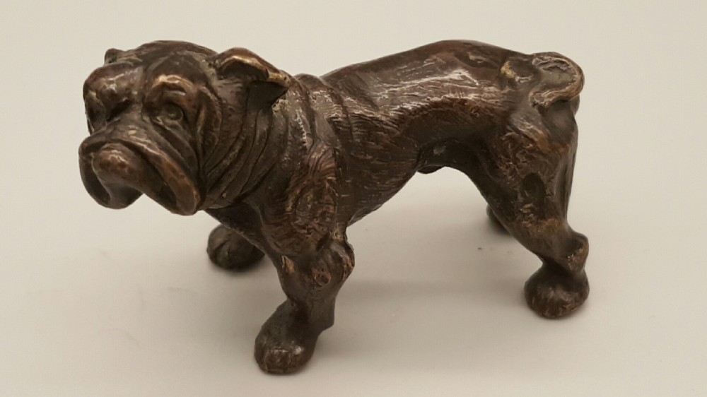 A small dark bronze figurine depicting a standing bulldog with detailed wrinkled facial features and a dark patinated finish.
