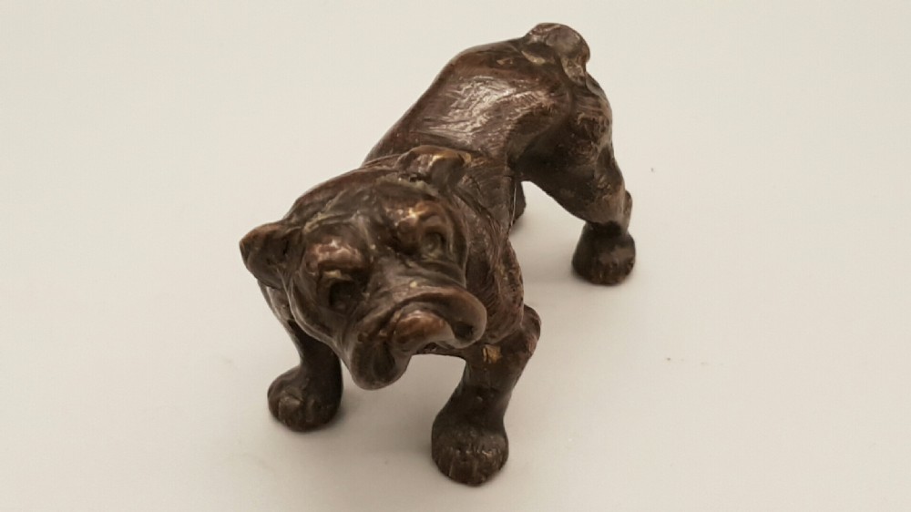 A small dark bronze figurine depicting a standing bulldog with detailed wrinkled facial features and a dark patinated finish. View II