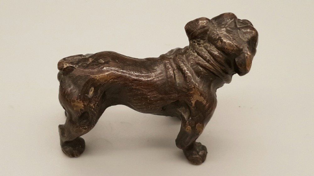 A small dark bronze figurine depicting a standing bulldog with detailed wrinkled facial features and a dark patinated finish. View III