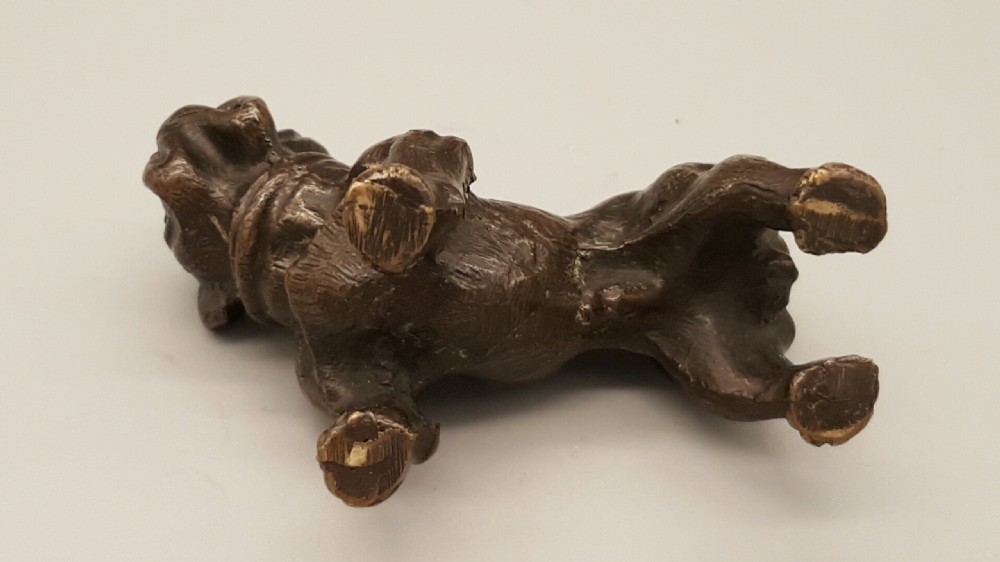 A small dark bronze figurine depicting a standing bulldog with detailed wrinkled facial features and a dark patinated finish. View V