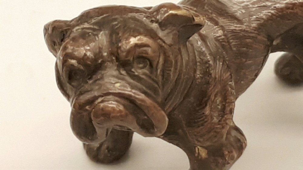 A small dark bronze figurine depicting a standing bulldog with detailed wrinkled facial features and a dark patinated finish. View VI