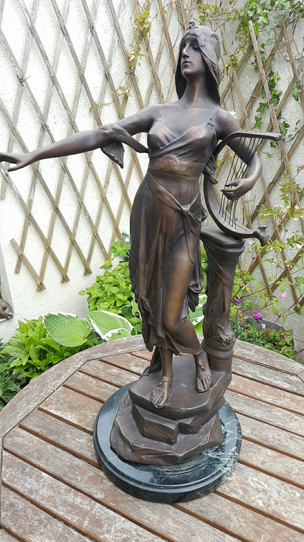 A dark patinated bronze sculpture of Salome draped in classical robes holding a lyre, positioned on a rounded dark marble base.