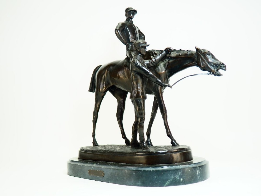 A dark patinated bronze equestrian sculpture depicting a jockey mounted on a racehorse accompanied by a standing groom, set upon an oval green marble base.