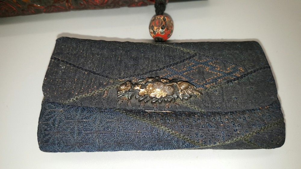 A Japanese Meiji period smoking ensemble featuring a dark woven silk tobacco pouch with a metal clasp beside a carved dark red-brown pipe case connected by a cord with an ojime bead. View III
