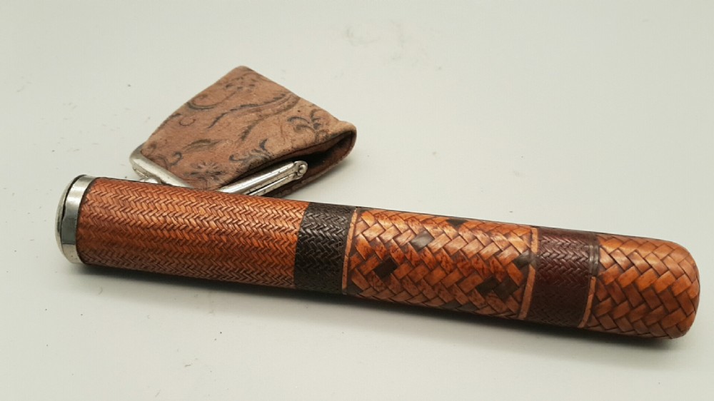 A Japanese woven bamboo pipe case with dark geometric weave bands paired with an attached pattern brocade purse.