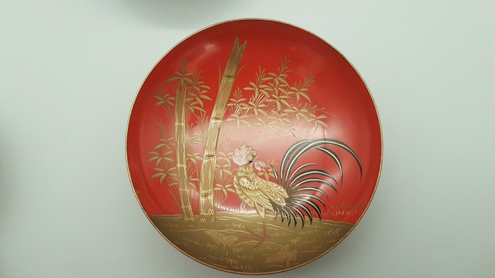 A set of four graduated Japanese red lacquer sake cups decorated with intricate gold maki-e illustrations including cranes, bamboo, and a rooster. View II