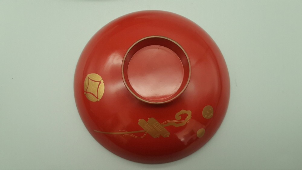 A set of four graduated Japanese red lacquer sake cups decorated with intricate gold maki-e illustrations including cranes, bamboo, and a rooster. View III