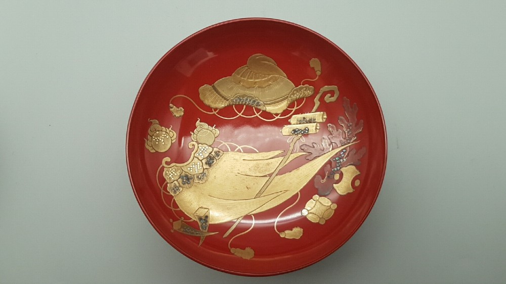 A set of four graduated Japanese red lacquer sake cups decorated with intricate gold maki-e illustrations including cranes, bamboo, and a rooster. View IV
