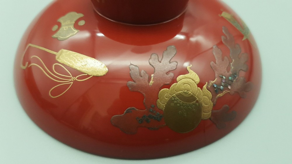 A set of four graduated Japanese red lacquer sake cups decorated with intricate gold maki-e illustrations including cranes, bamboo, and a rooster. View V