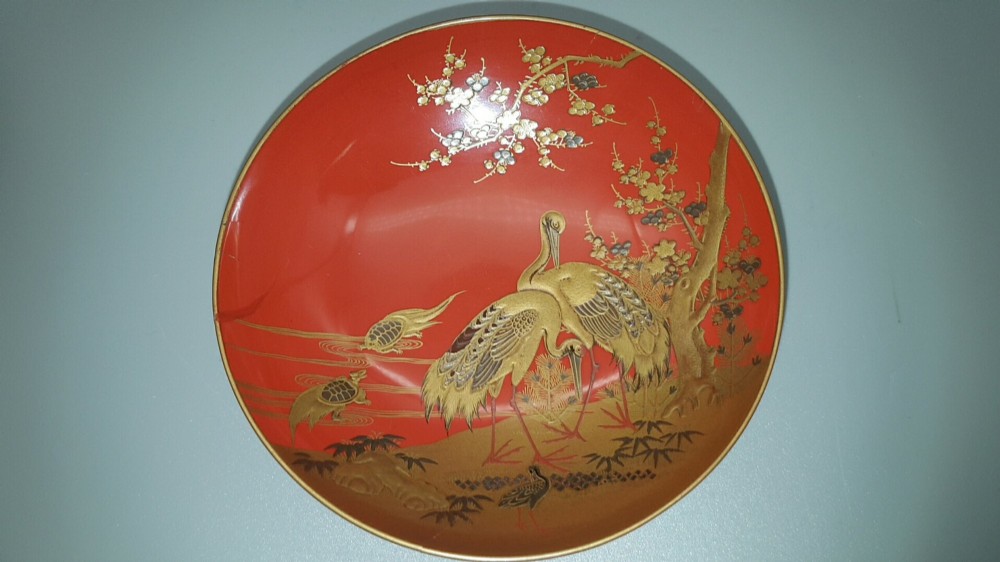 A set of four graduated Japanese red lacquer sake cups decorated with intricate gold maki-e illustrations including cranes, bamboo, and a rooster. View VI