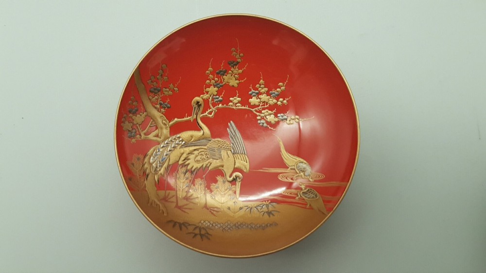 A set of four graduated Japanese red lacquer sake cups decorated with intricate gold maki-e illustrations including cranes, bamboo, and a rooster. View VII