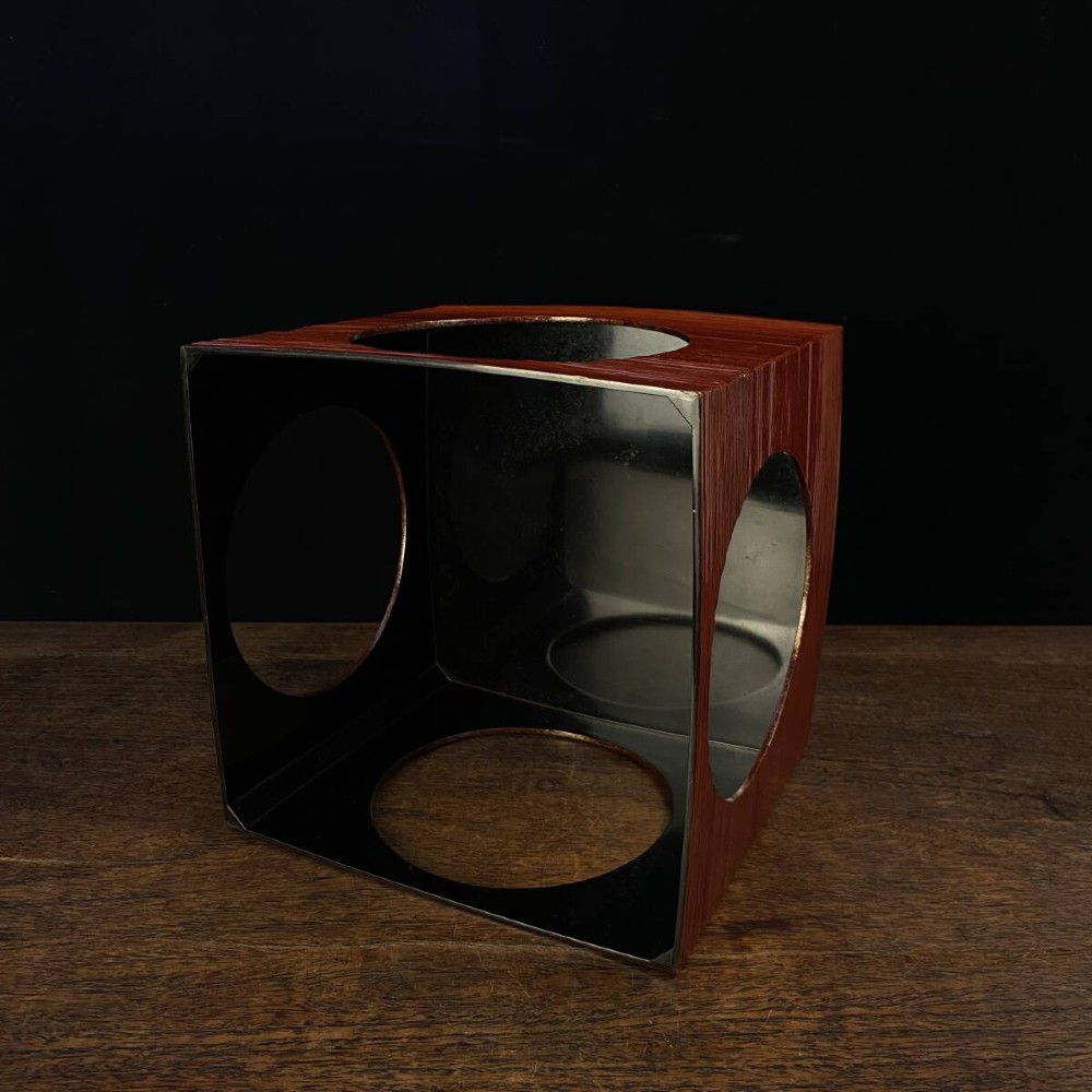 A large red lacquer Japanese sake cup decorated with gold maki-e motifs resting atop a dark brown wooden lacquer stand with a circular cutout. View VIII