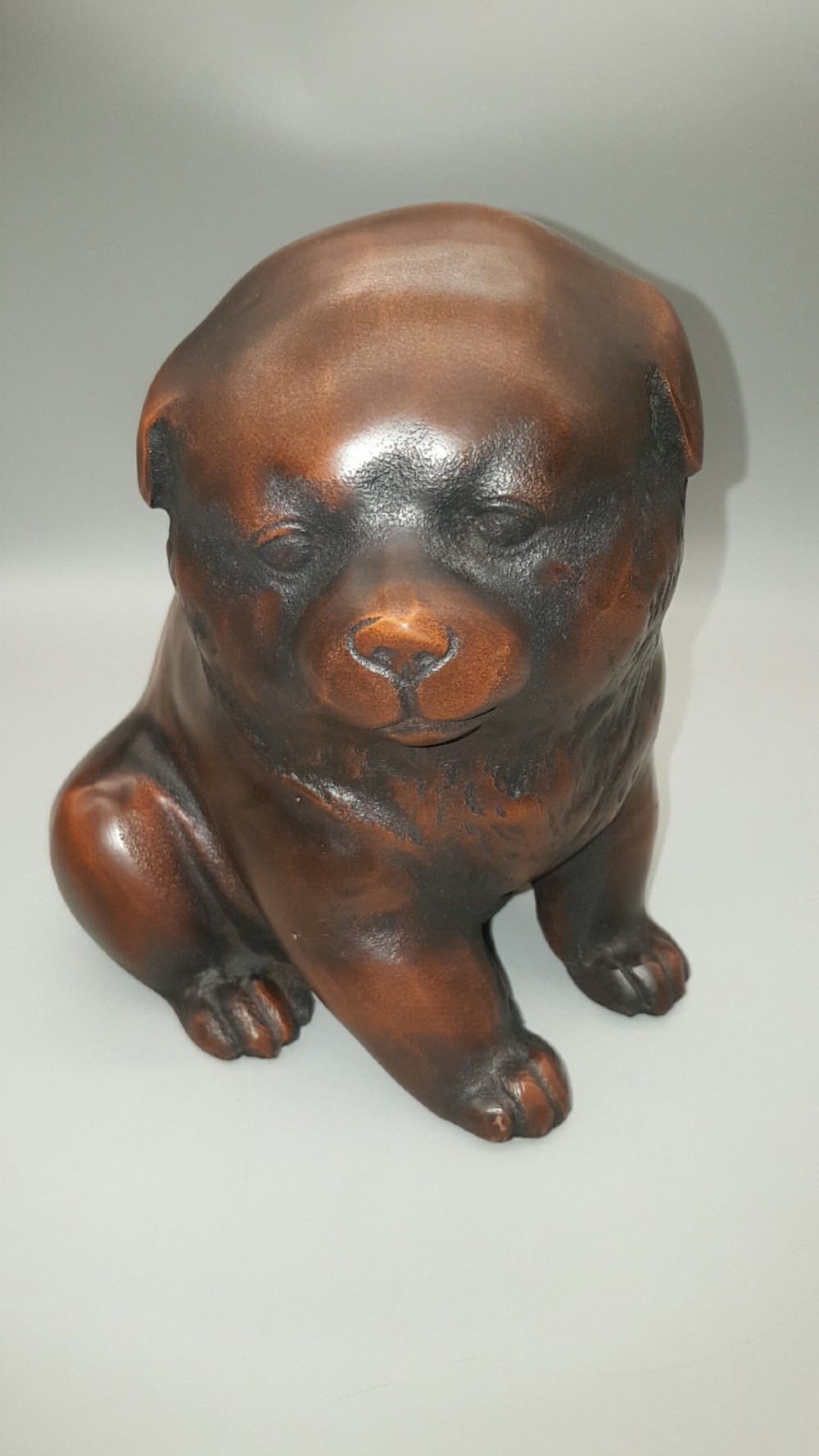 A cast bronze sculpture depicting a seated puppy with a warm brown patina and dark accents around its face.