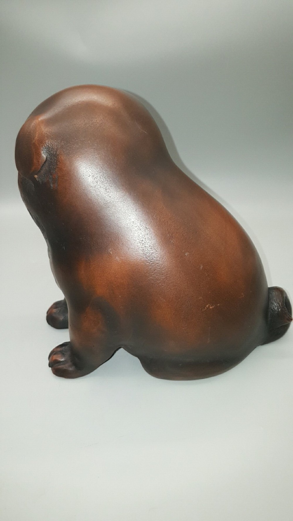 A cast bronze sculpture depicting a seated puppy with a warm brown patina and dark accents around its face. View IV