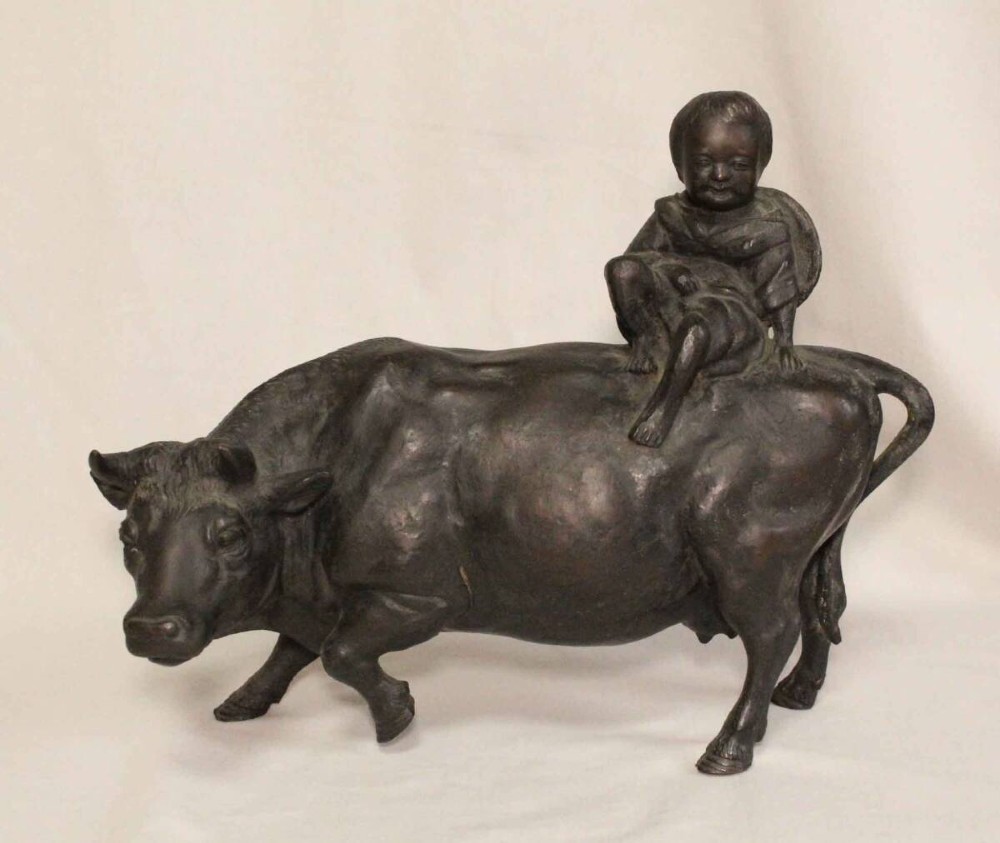 A late nineteenth-century Japanese cast bronze sculpture depicting a young boy seated atop a walking ox with a dark brown patina. View II