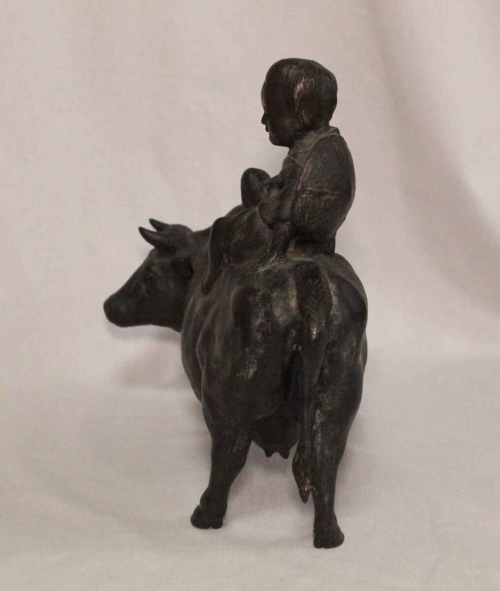 A late nineteenth-century Japanese cast bronze sculpture depicting a young boy seated atop a walking ox with a dark brown patina. View V