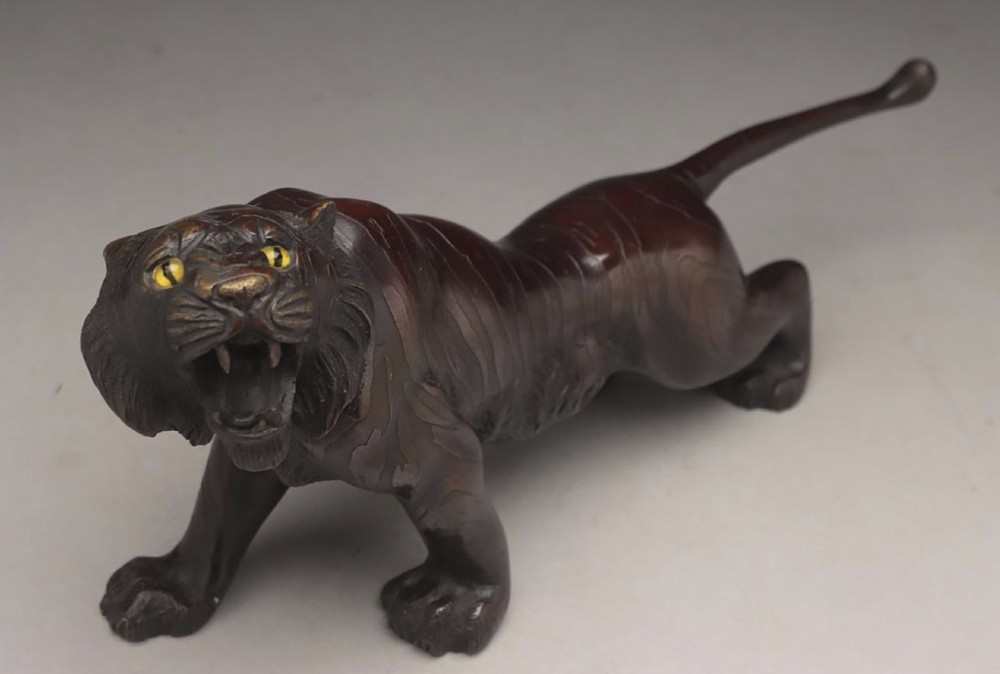 A dark patinated bronze sculpture depicting a snarling tiger in a low prowling stance with inset yellow crystal eyes.