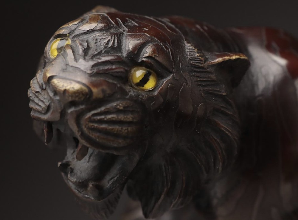 A dark patinated bronze sculpture depicting a snarling tiger in a low prowling stance with inset yellow crystal eyes. View VI