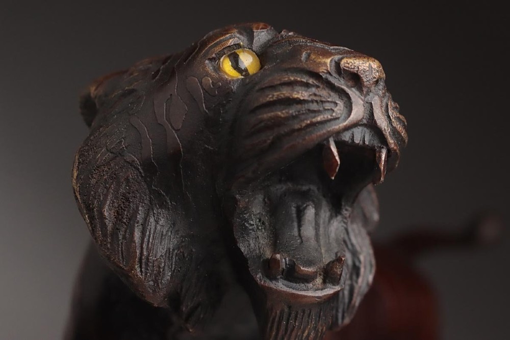 A dark patinated bronze sculpture depicting a snarling tiger in a low prowling stance with inset yellow crystal eyes. View VII