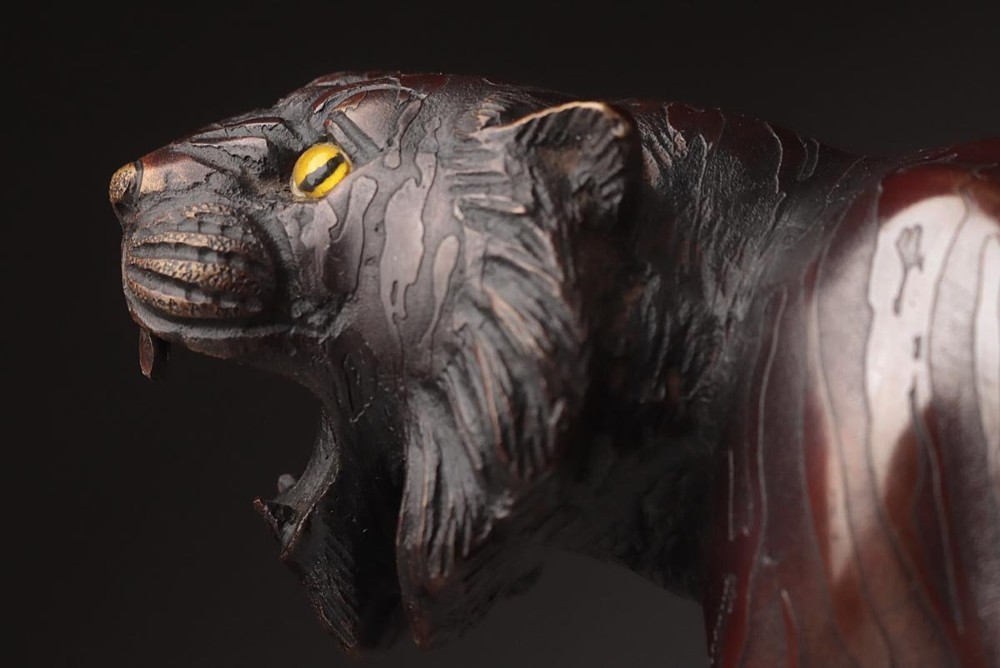 A dark patinated bronze sculpture depicting a snarling tiger in a low prowling stance with inset yellow crystal eyes. View VIII