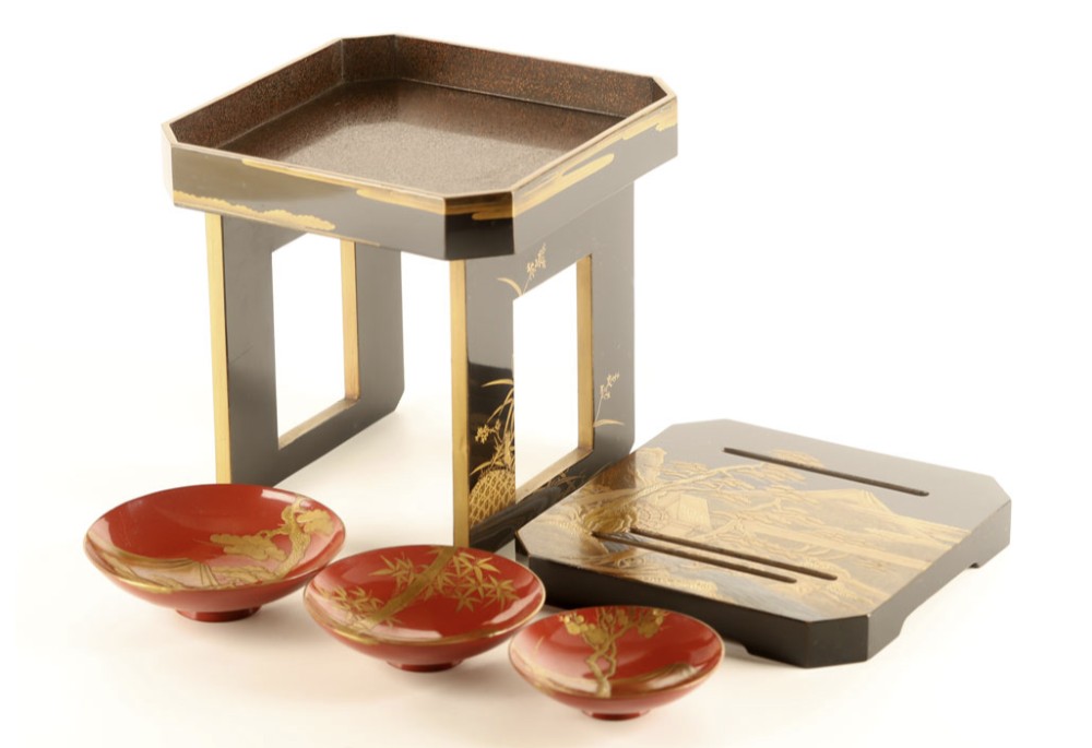 A Japanese black and gold lacquerware sake table featuring a raised stand, removable matching tray, and three red lacquer sakazuki cups adorned with painted gold motifs.
