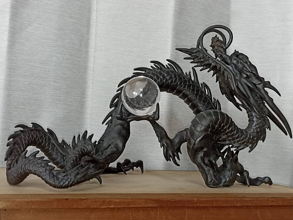 A late 19th-century Japanese dark bronze dragon sculpture holding a clear glass sphere along its serpentine body.