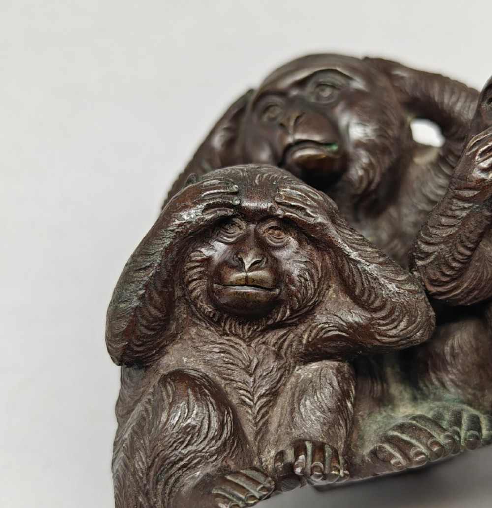 A patinated dark bronze sculpture depicting three monkeys seated together representing the motif of see no evil, hear no evil, and speak no evil. View III