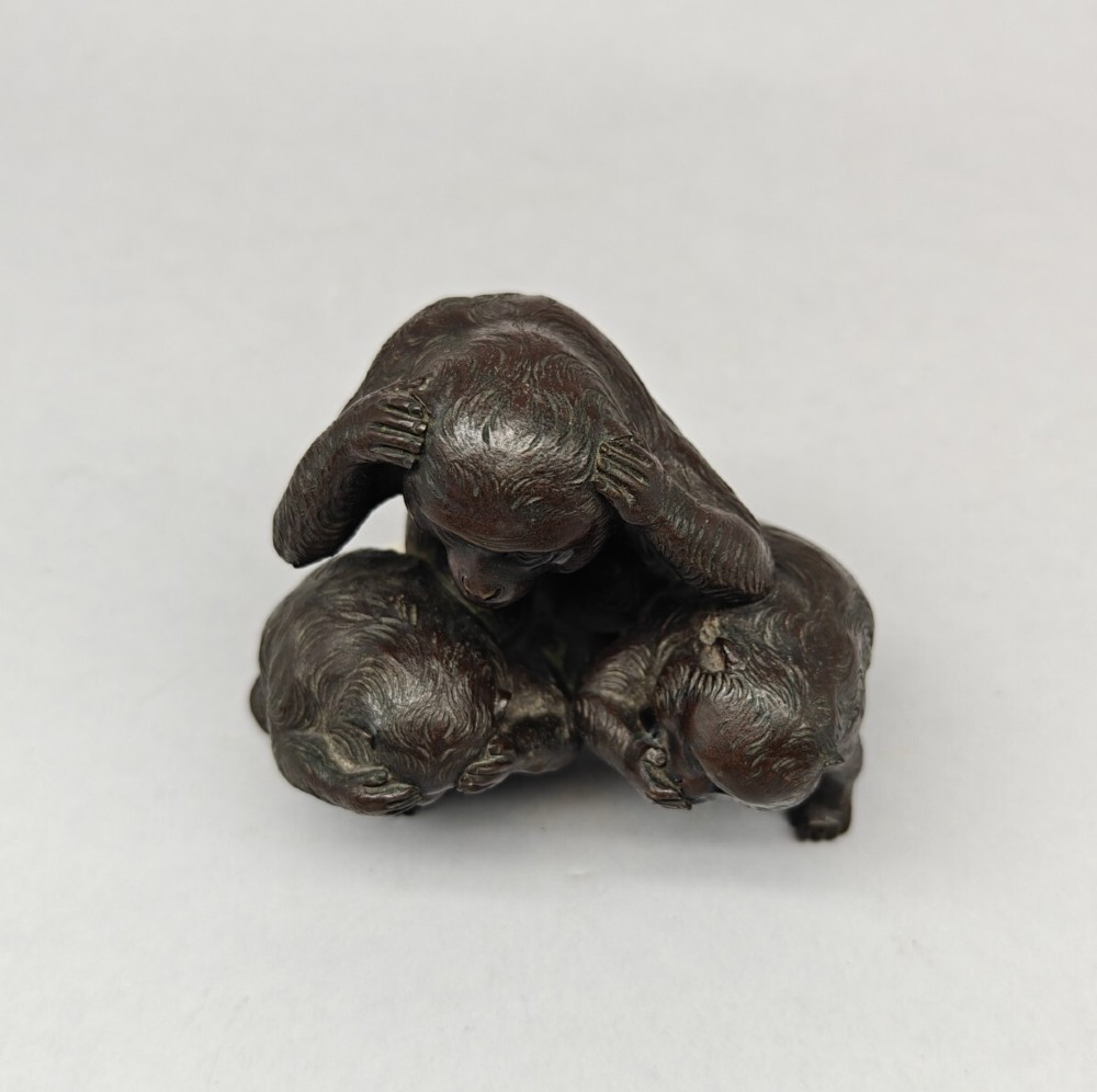 A patinated dark bronze sculpture depicting three monkeys seated together representing the motif of see no evil, hear no evil, and speak no evil. View VI