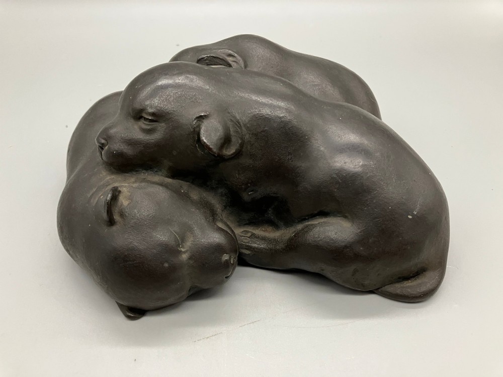 A dark patinated bronze sculpture depicting three sleeping puppies curled closely together.