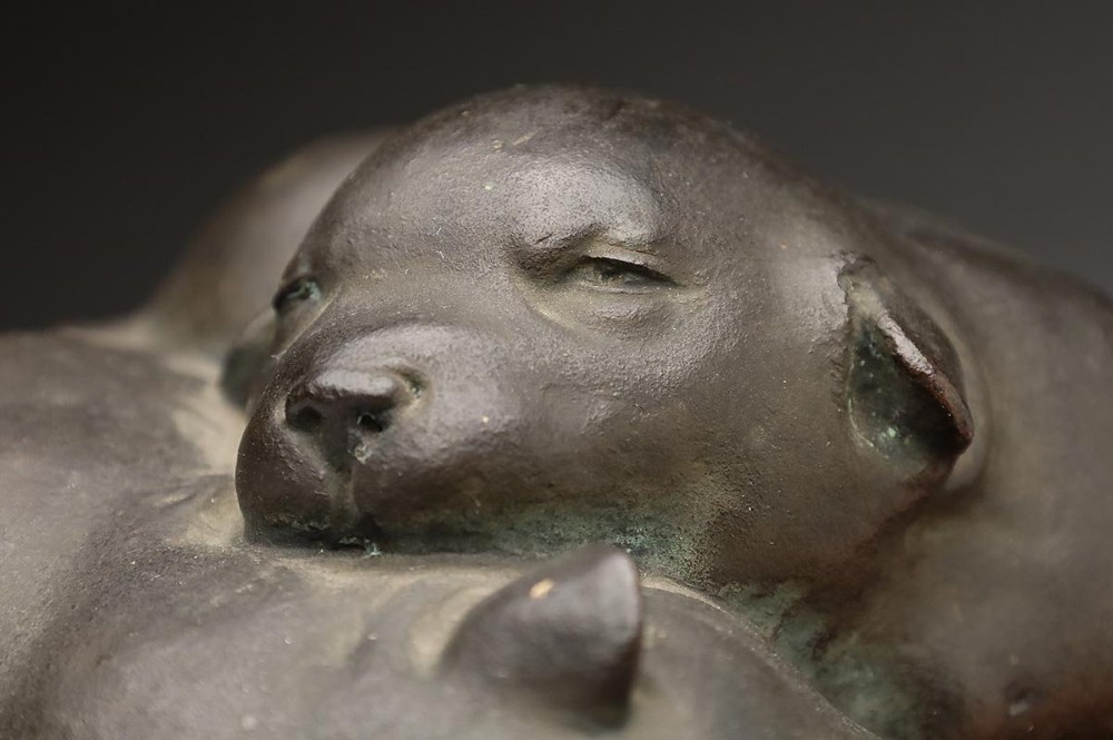 A dark patinated bronze sculpture depicting three sleeping puppies curled closely together. View II