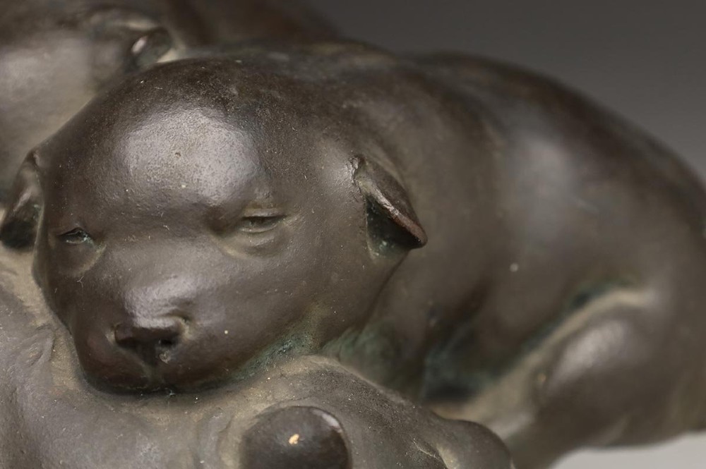 A dark patinated bronze sculpture depicting three sleeping puppies curled closely together. View IV