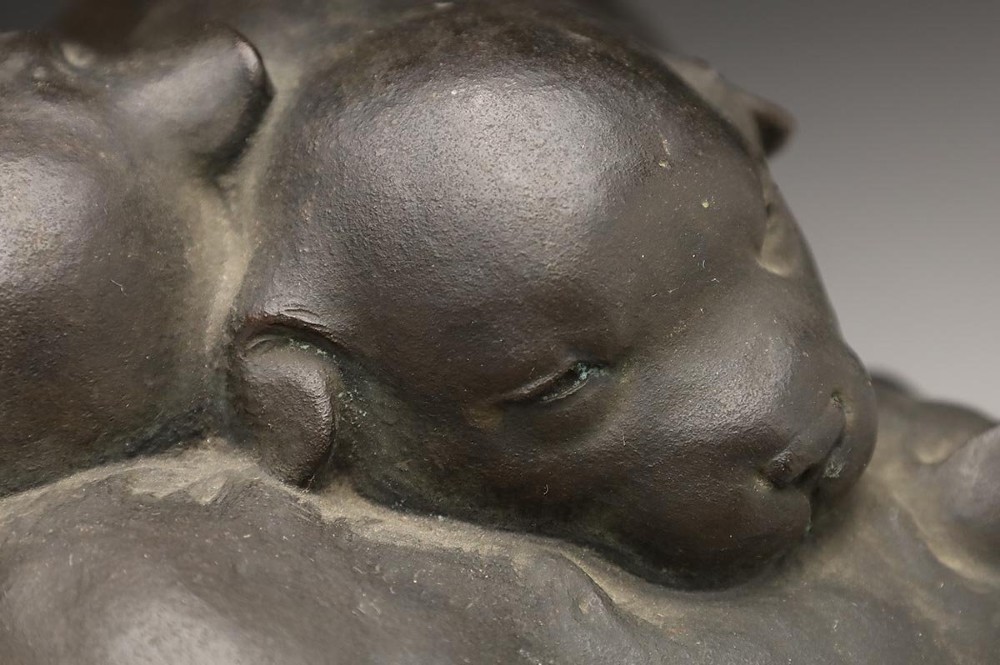 A dark patinated bronze sculpture depicting three sleeping puppies curled closely together. View VI
