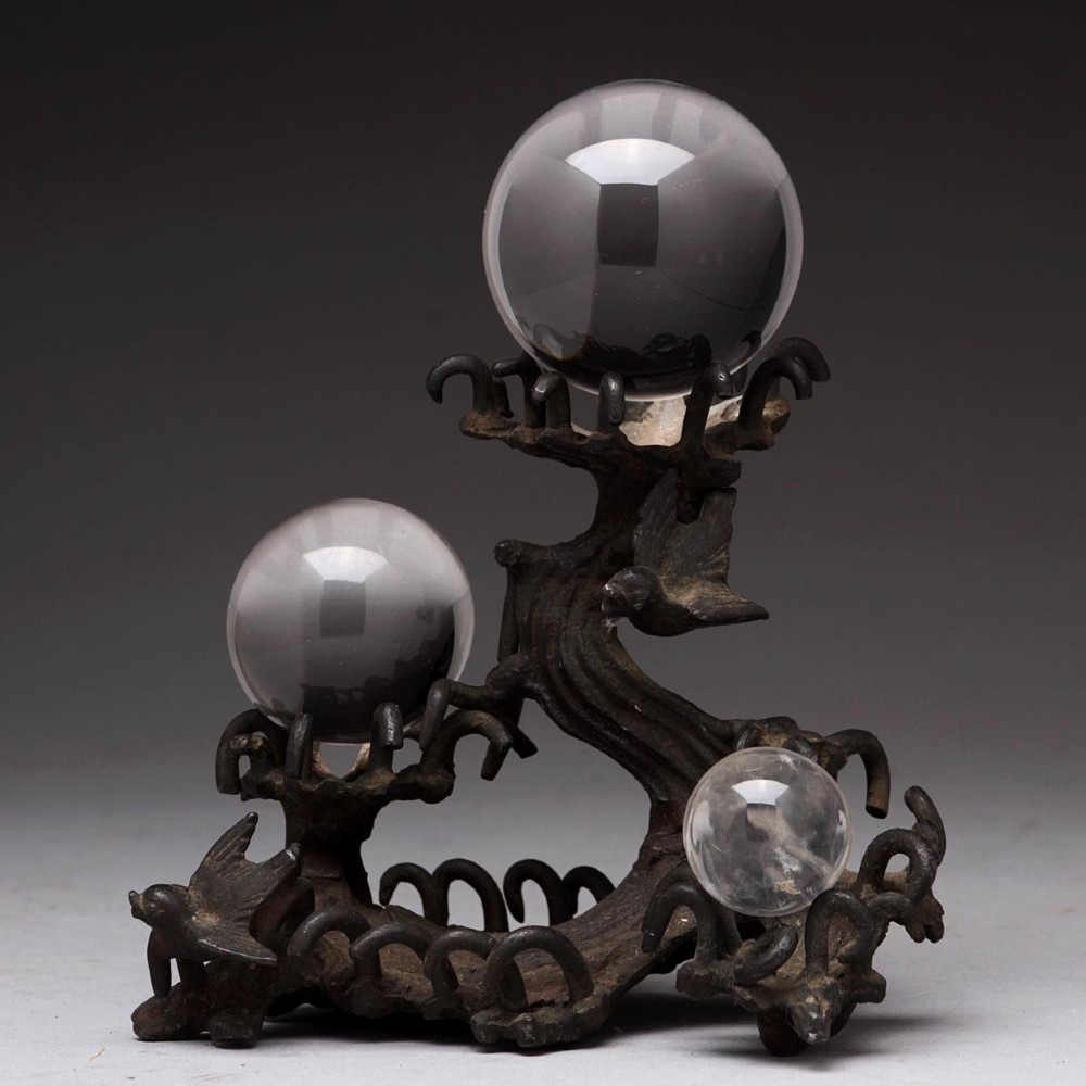 A dark patinated bronze Japanese Meiji period wave stand holding three clear crystal spheres at different elevations.