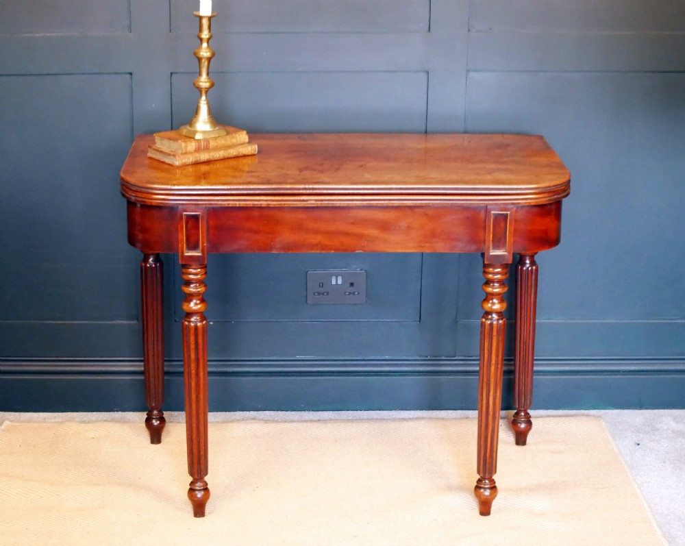 A nineteenth-century William IV mahogany fold-over tea table featuring reeded turned legs and a polished timber surface.