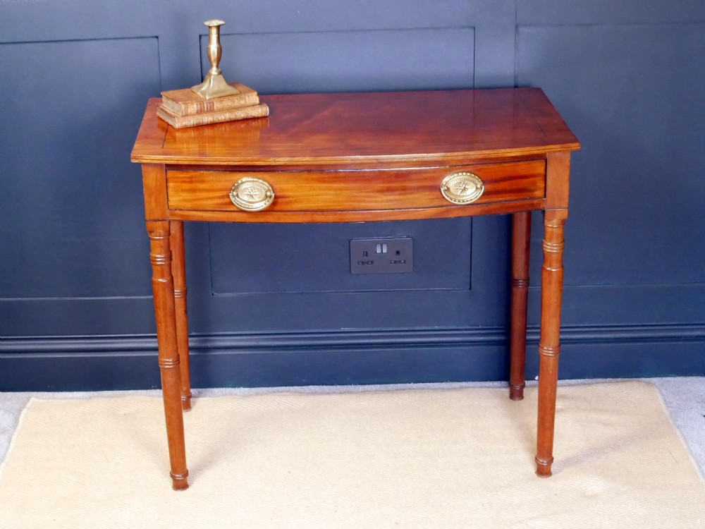 A Regency mahogany demi-lune side table featuring a single drawer with oval brass handles and four slender turned legs.