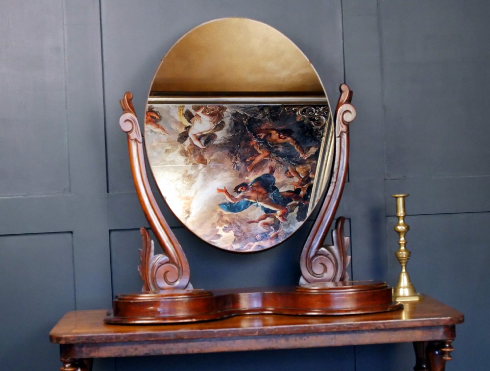 A Victorian mahogany dressing mirror featuring an oval tilting glass plate set between carved scroll uprights on a shaped plinth base.